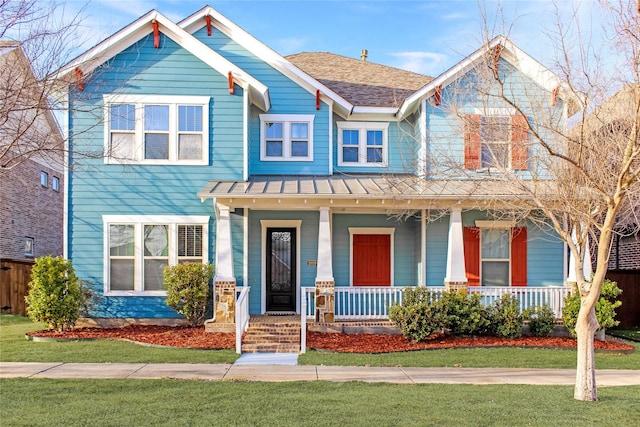 craftsman-style home with a porch, a front lawn, a shingled roof, and fence