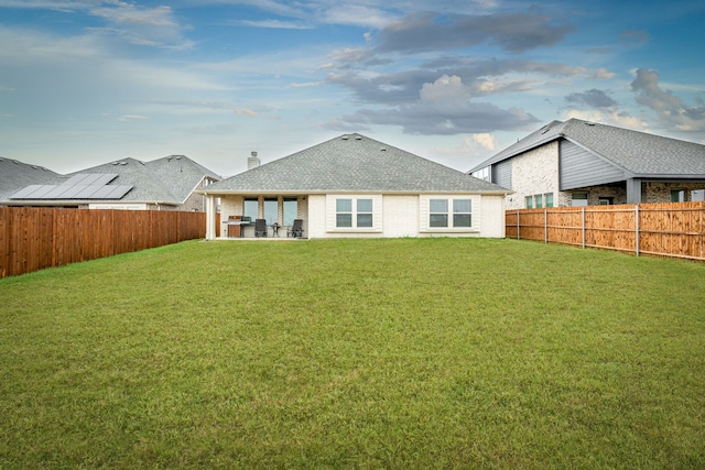 rear view of house featuring roof with shingles, a chimney, a fenced backyard, a yard, and a patio area