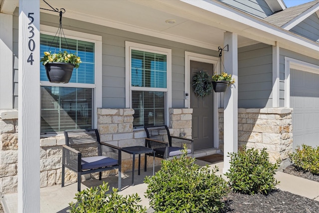 property entrance with covered porch, stone siding, and an attached garage