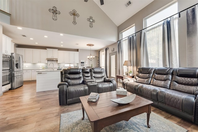 living room featuring high vaulted ceiling, light wood-type flooring, visible vents, and a notable chandelier