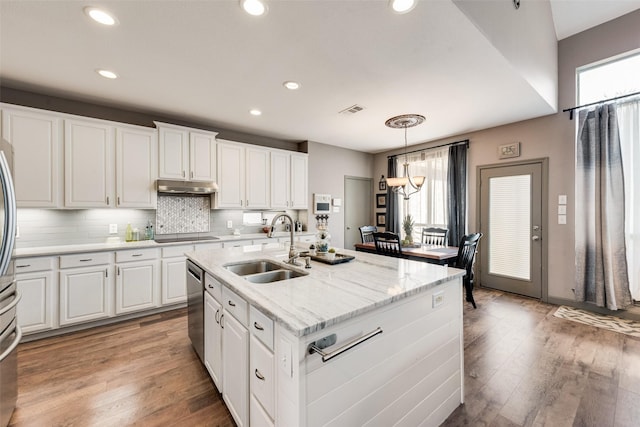 kitchen with light wood finished floors, stainless steel appliances, white cabinets, a sink, and under cabinet range hood