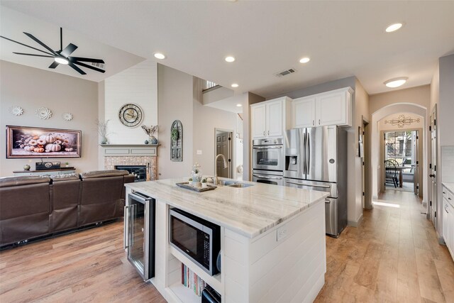 kitchen with arched walkways, wine cooler, light stone countertops, stainless steel appliances, and a sink