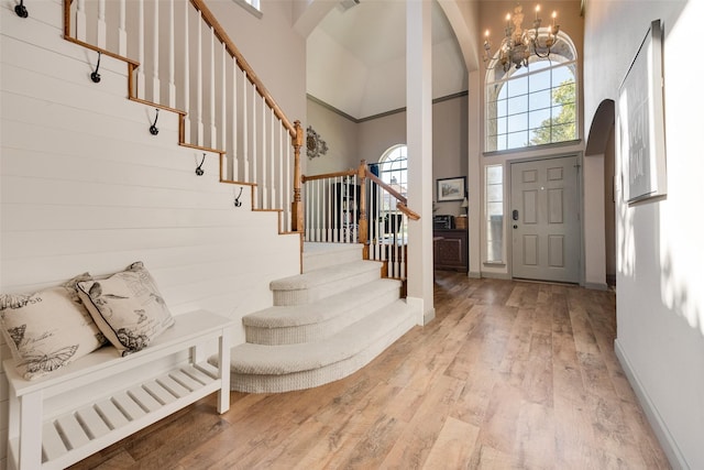 foyer entrance with light wood finished floors, visible vents, a towering ceiling, stairs, and a chandelier