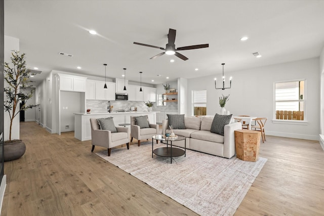 living room featuring light wood-style floors, recessed lighting, visible vents, and ceiling fan with notable chandelier