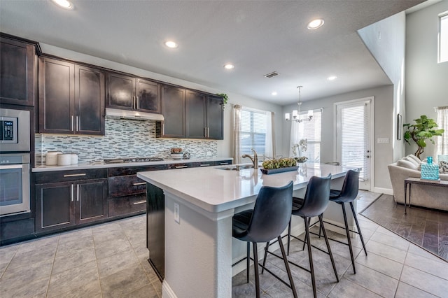 kitchen with visible vents, a breakfast bar area, stainless steel appliances, under cabinet range hood, and a sink