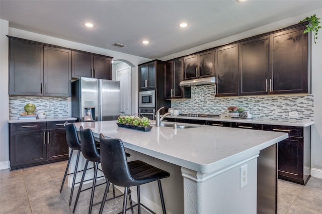 kitchen with arched walkways, appliances with stainless steel finishes, a breakfast bar, under cabinet range hood, and a sink