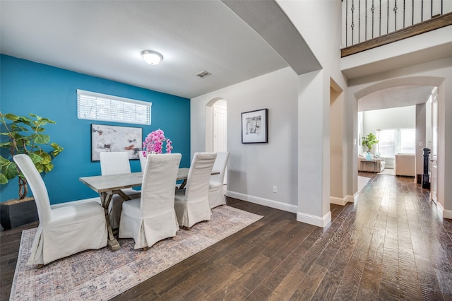 dining space featuring arched walkways, dark wood finished floors, visible vents, and baseboards