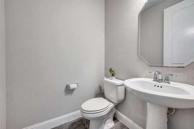 bathroom featuring a textured wall, a sink, toilet, and baseboards