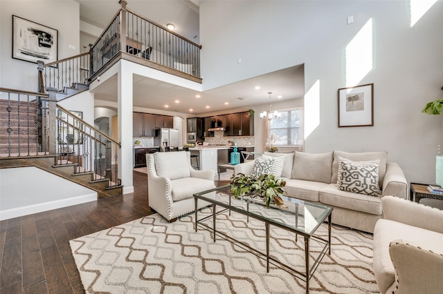 living room featuring a notable chandelier, dark wood-type flooring, a towering ceiling, baseboards, and stairway