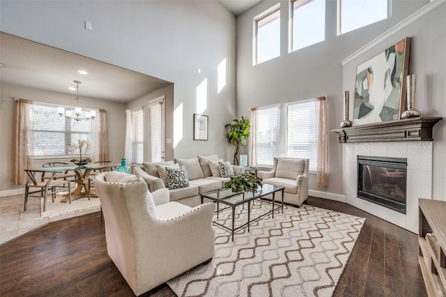 living area with baseboards, a tile fireplace, a towering ceiling, dark wood-style flooring, and a chandelier