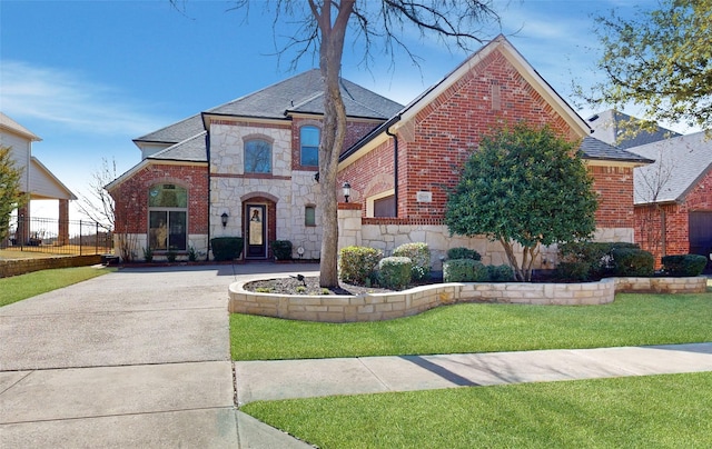 french country home featuring brick siding, a shingled roof, fence, stone siding, and a front lawn