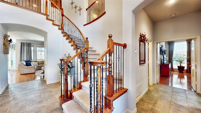 stairs featuring arched walkways, visible vents, a towering ceiling, stone finish flooring, and baseboards