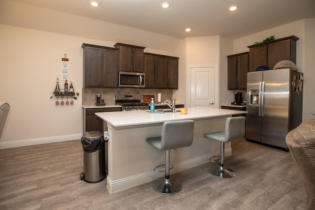 kitchen featuring stainless steel appliances, light countertops, light wood finished floors, and dark brown cabinets