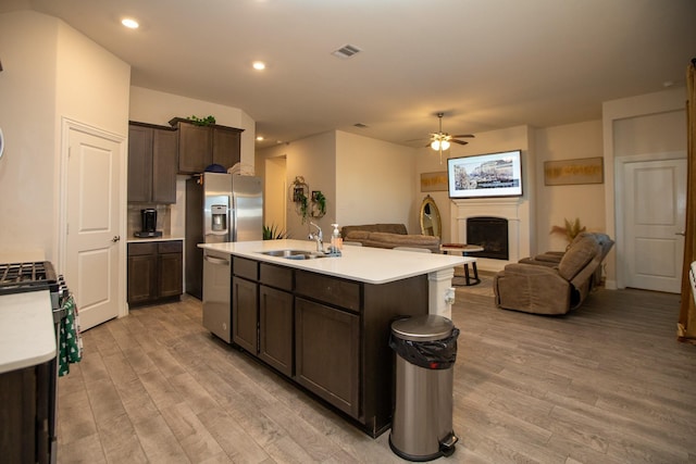 kitchen with stainless steel appliances, a fireplace with raised hearth, a sink, and light wood finished floors