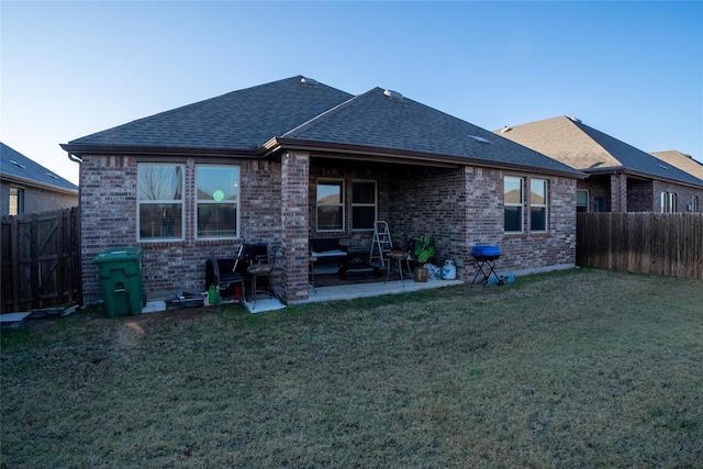 back of house featuring a shingled roof, brick siding, a yard, and a patio