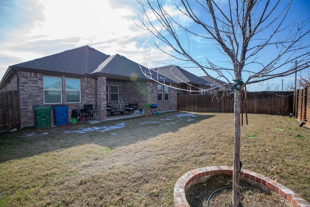 back of house with brick siding, a fenced backyard, a shingled roof, and a yard