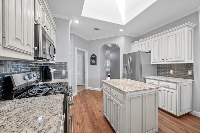 kitchen featuring visible vents, arched walkways, wood finished floors, a center island, and stainless steel appliances