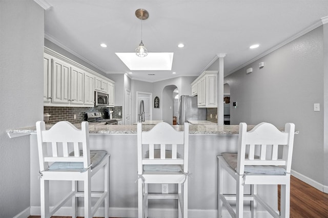 kitchen featuring stainless steel appliances, ornamental molding, backsplash, and a peninsula