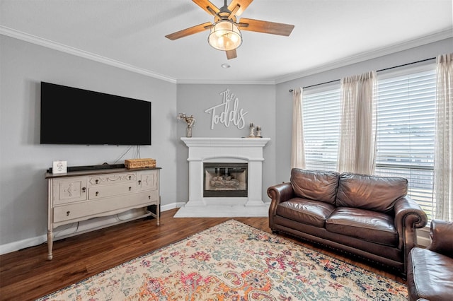 living room featuring ceiling fan, wood finished floors, baseboards, ornamental molding, and a glass covered fireplace