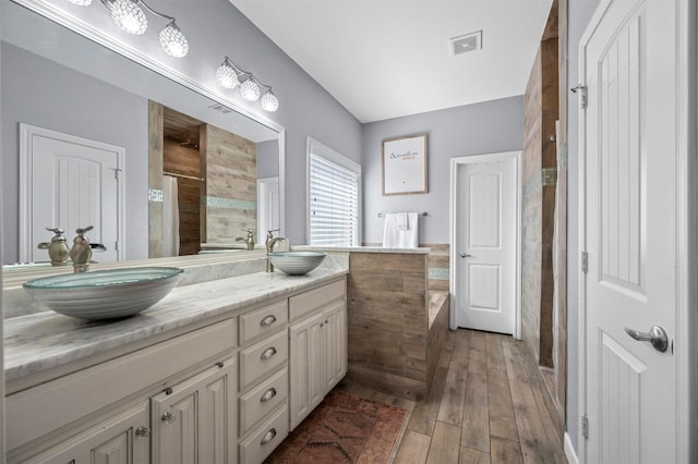 bathroom with double vanity, visible vents, a sink, and tiled shower