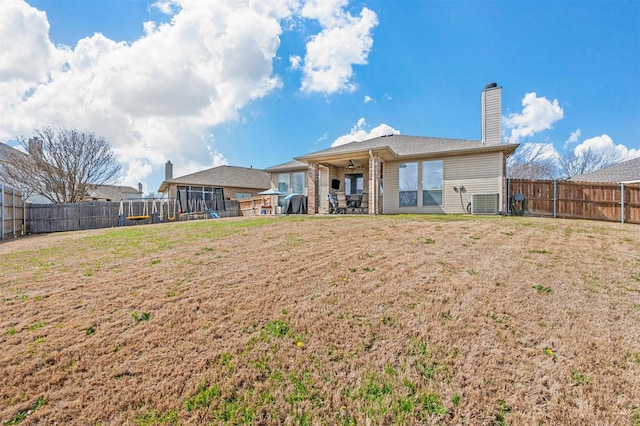 rear view of house featuring a fenced backyard, a chimney, and a lawn