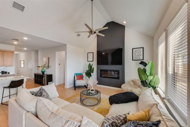 living room featuring light wood-type flooring, a glass covered fireplace, and visible vents