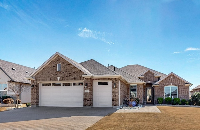 view of front of house with brick siding, roof with shingles, an attached garage, decorative driveway, and a front yard