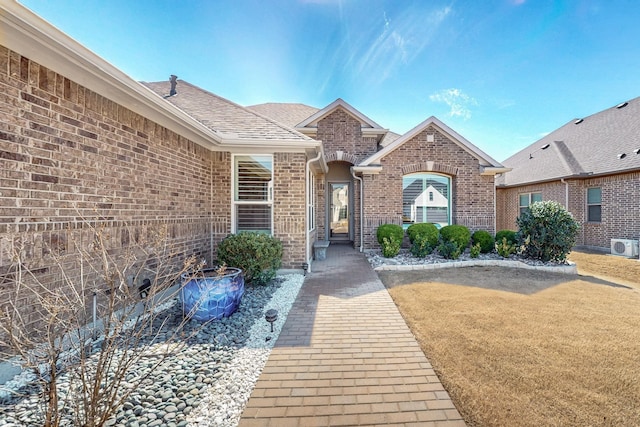 doorway to property featuring roof with shingles, a lawn, and brick siding