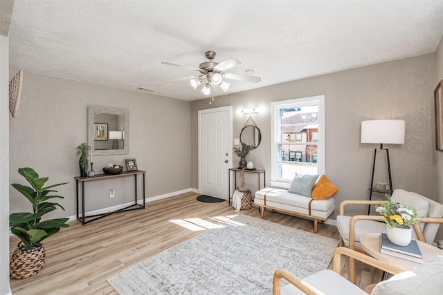 living room with a textured ceiling, a ceiling fan, visible vents, baseboards, and light wood-type flooring