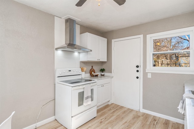 kitchen with white range with electric stovetop, light wood finished floors, light countertops, white cabinets, and wall chimney range hood