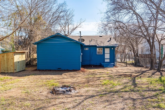 back of house with a shingled roof, entry steps, fence, and an outbuilding