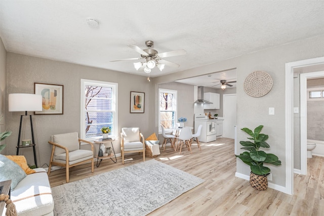 living area featuring light wood-style floors, a ceiling fan, baseboards, and a textured ceiling