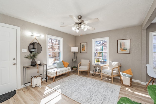 living area featuring light wood-type flooring, baseboards, a ceiling fan, and a textured wall