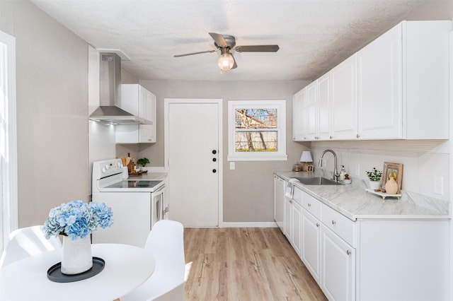 kitchen with white appliances, a sink, white cabinetry, light wood-style floors, and wall chimney range hood