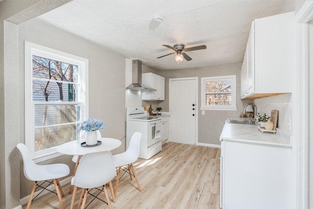 kitchen with electric stove, wall chimney exhaust hood, light wood-style flooring, light countertops, and a sink