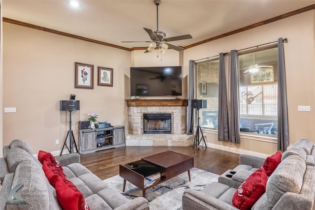 living area with ornamental molding, a ceiling fan, a stone fireplace, wood finished floors, and baseboards