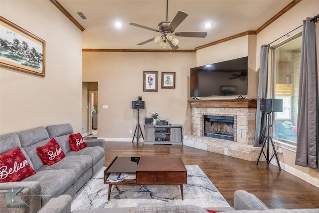 living room featuring visible vents, ornamental molding, a stone fireplace, wood finished floors, and baseboards