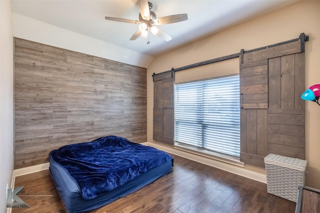 bedroom featuring a barn door, baseboards, a ceiling fan, wood finished floors, and vaulted ceiling