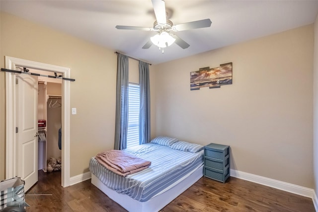 bedroom with wood finished floors, a spacious closet, baseboards, and a barn door