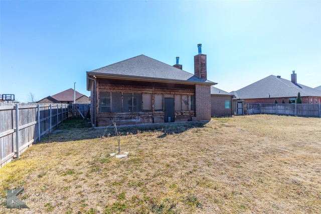 back of house featuring brick siding, a fenced backyard, a chimney, and a yard