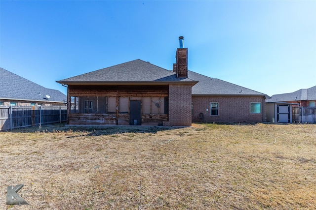 back of house with a chimney, roof with shingles, fence, a yard, and brick siding