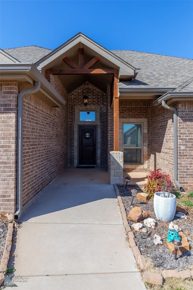 view of exterior entry featuring brick siding and roof with shingles