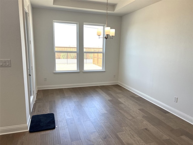 unfurnished dining area featuring an inviting chandelier, baseboards, a tray ceiling, and dark wood-style flooring