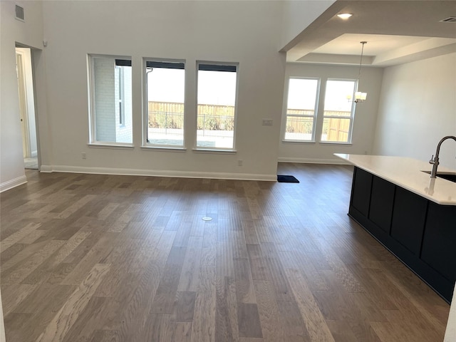 interior space with baseboards, visible vents, a raised ceiling, dark wood-style floors, and an inviting chandelier