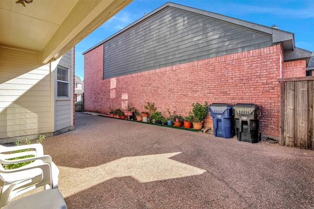 view of side of home featuring a patio area, fence, and brick siding