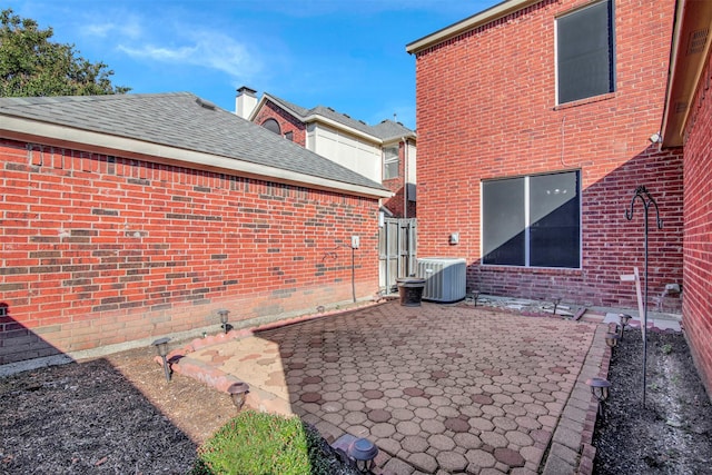 exterior space with a shingled roof, a patio area, central AC, and brick siding