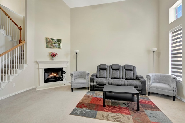 carpeted living area featuring stairway, a warm lit fireplace, a towering ceiling, and baseboards