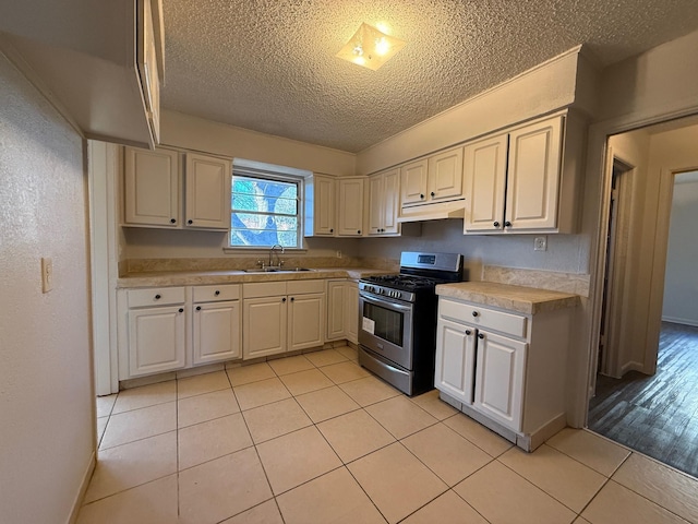 kitchen featuring stainless steel gas range oven, light tile patterned flooring, under cabinet range hood, a sink, and light countertops