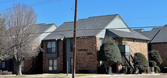 exterior space featuring roof with shingles, brick siding, stairway, and central air condition unit