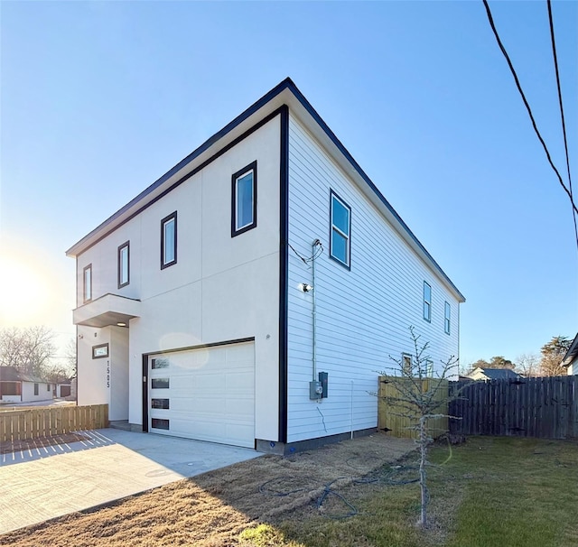 exterior space featuring concrete driveway, an attached garage, fence, and stucco siding